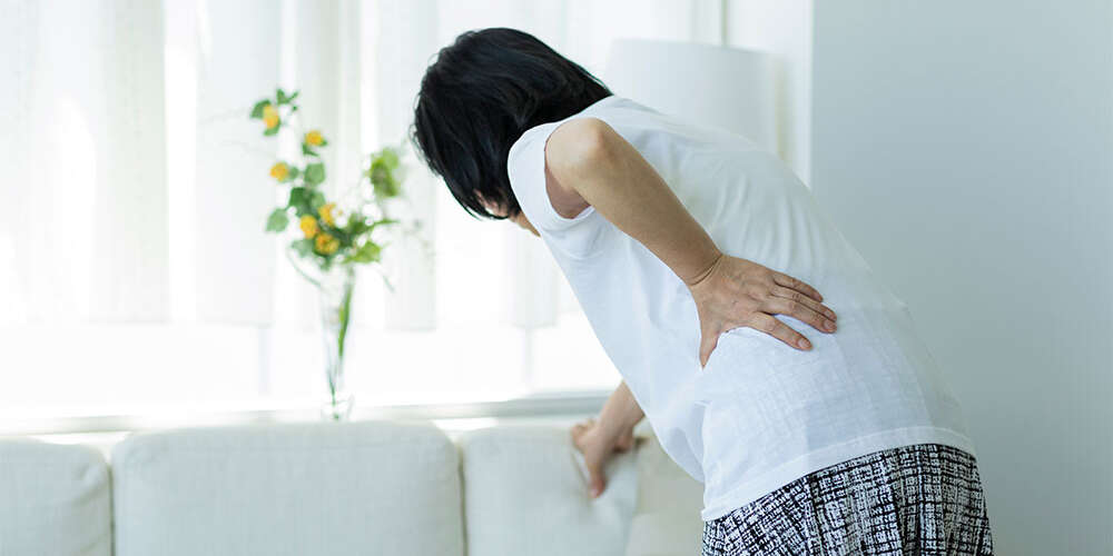 donna con mal di schiena si regge al divano